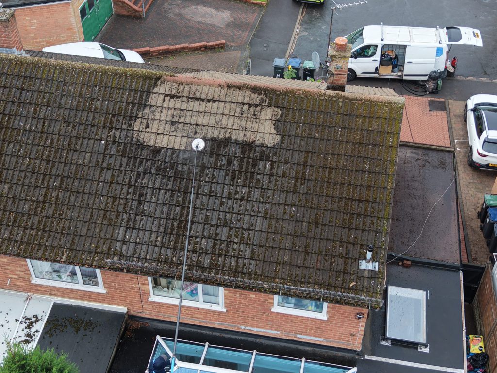 Aerial view of a moss-covered roof with the first section cleaned